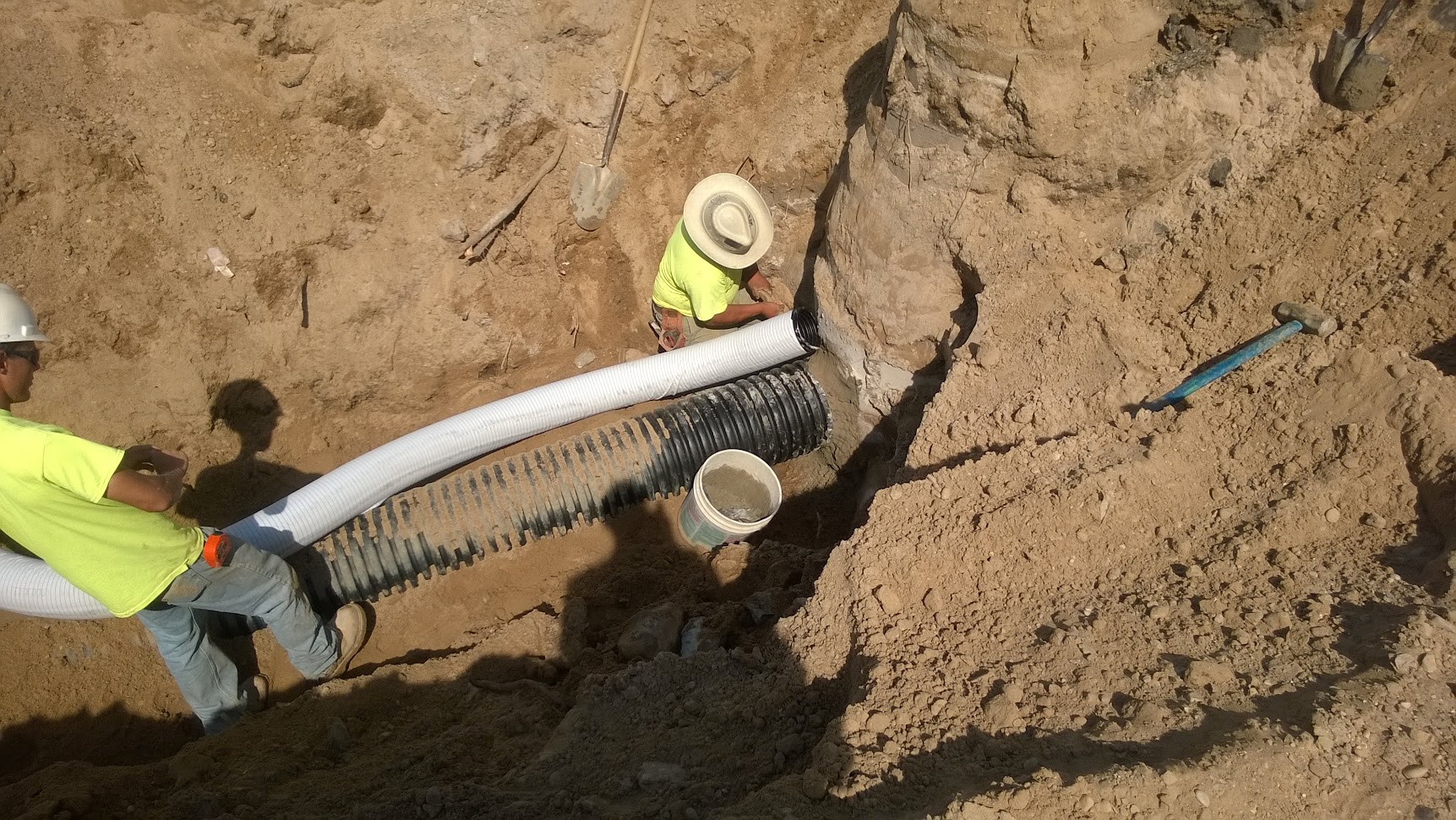 Close-up of stormwater drainage pipe being installed in excavated trench with workers in PPE — drainage and flood control engineering